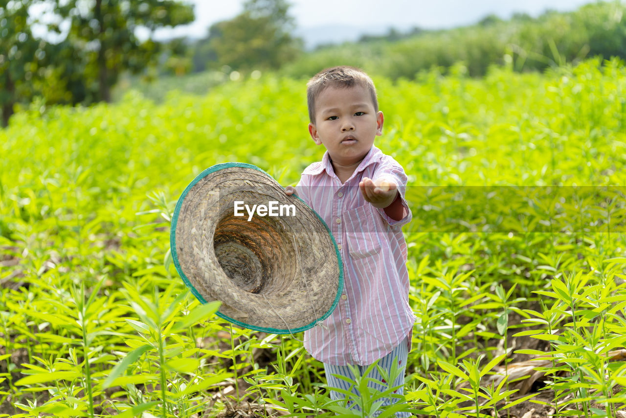 Portrait of boy holding hat while standing on field