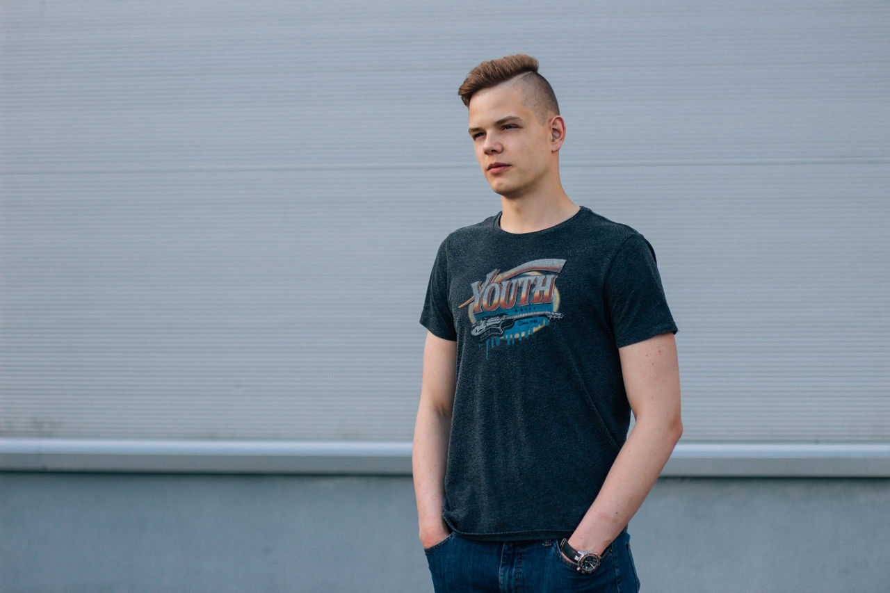 Confident young man with hands in pockets standing against wall