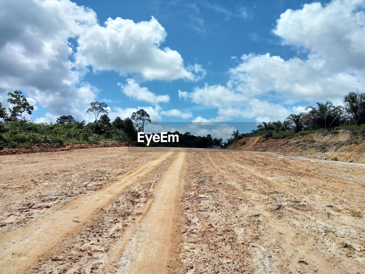 Dirt road amidst field against sky