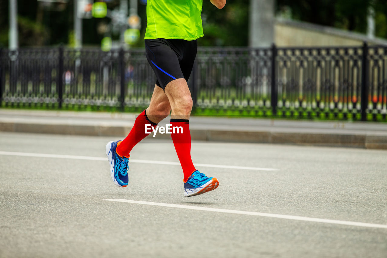 Legs male runner in bright red compression socks run down street race