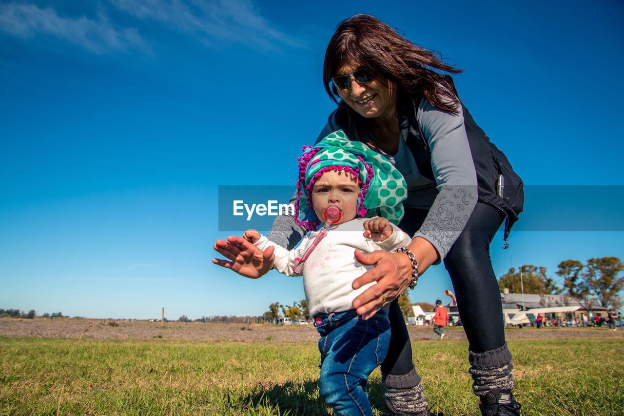 Mother and daughter on grass against sky