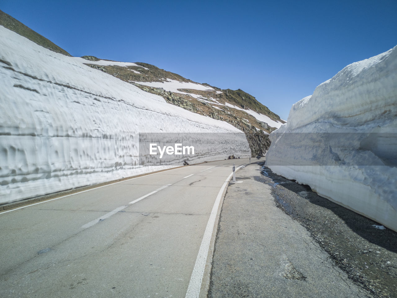 Road amidst snowcapped mountains against clear sky