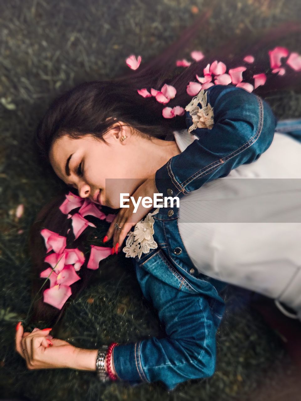 High angle view of woman with rose petals on hair lying over grass 