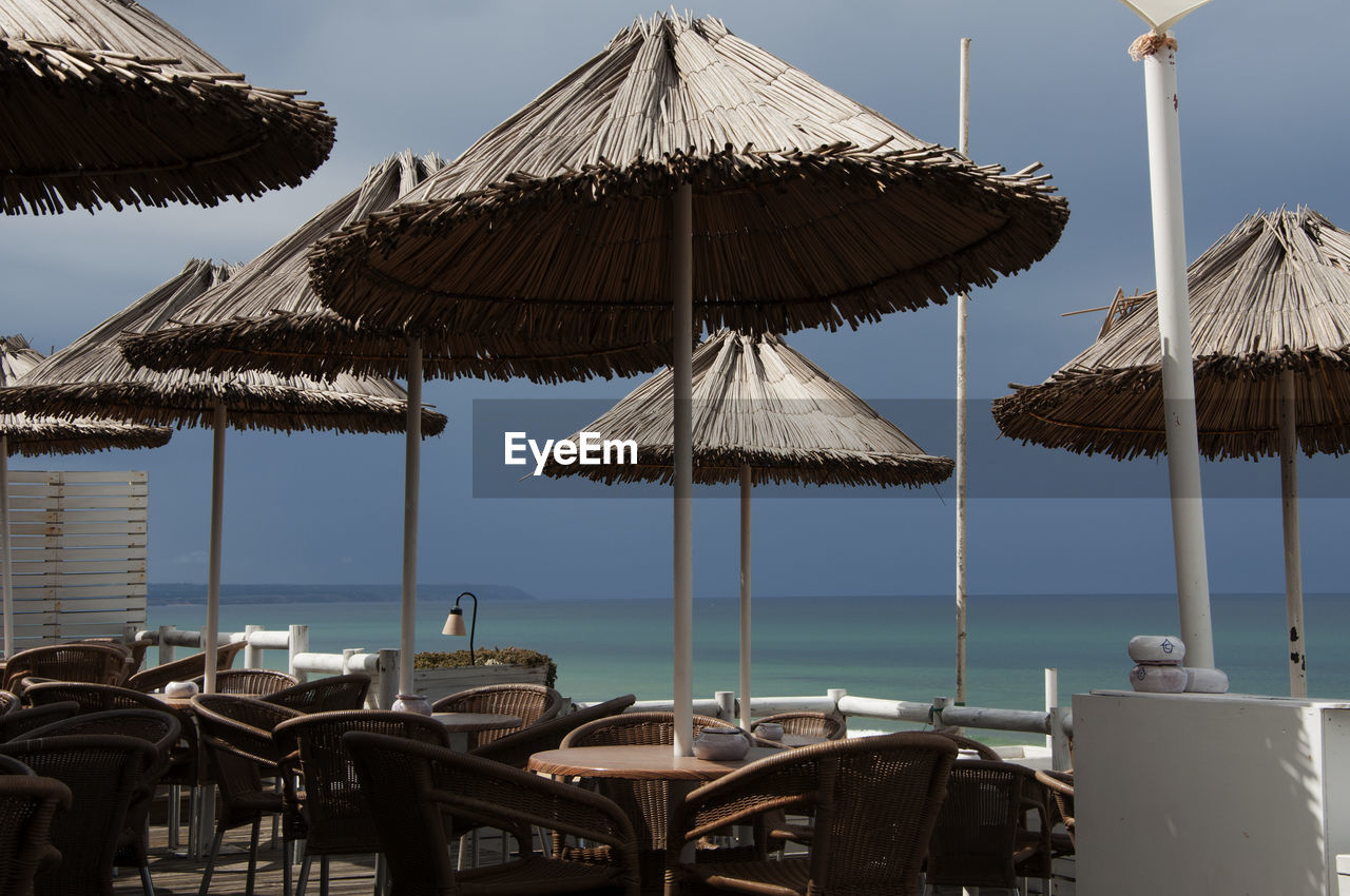 Chairs and parasol at restaurant by sea against sky