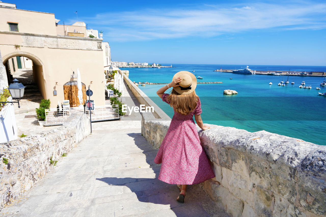 Rear view of woman standing by sea against sky