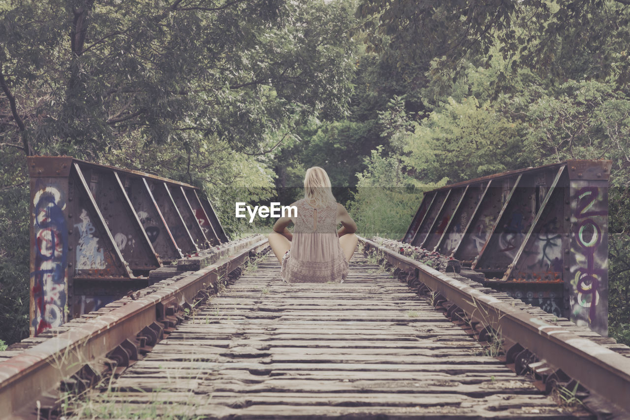 Rear view of woman sitting on old bridge in forest