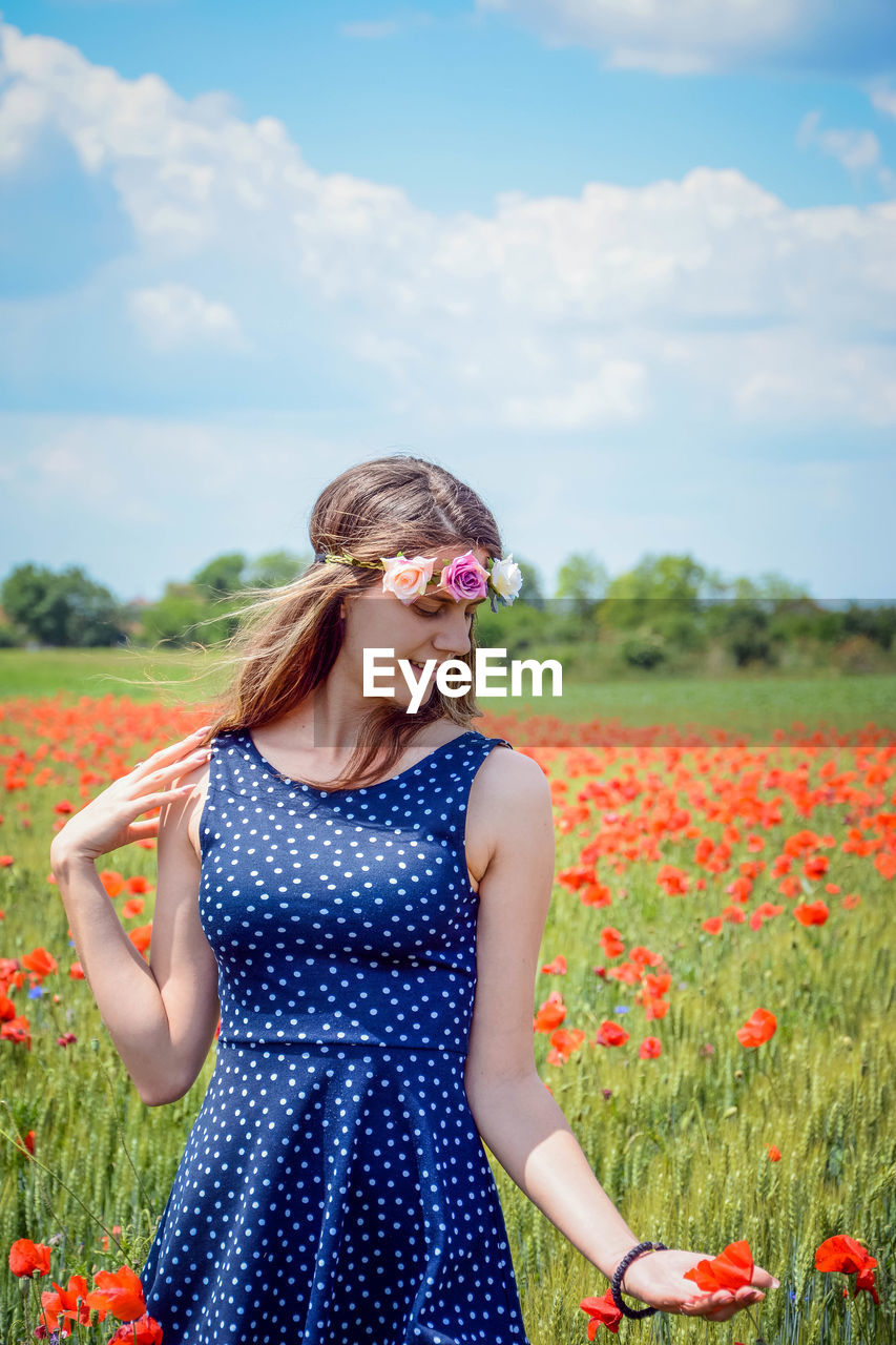 Young woman standing on field against sky