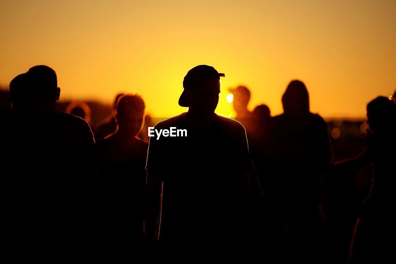 Silhouette people standing on field against clear orange sky
