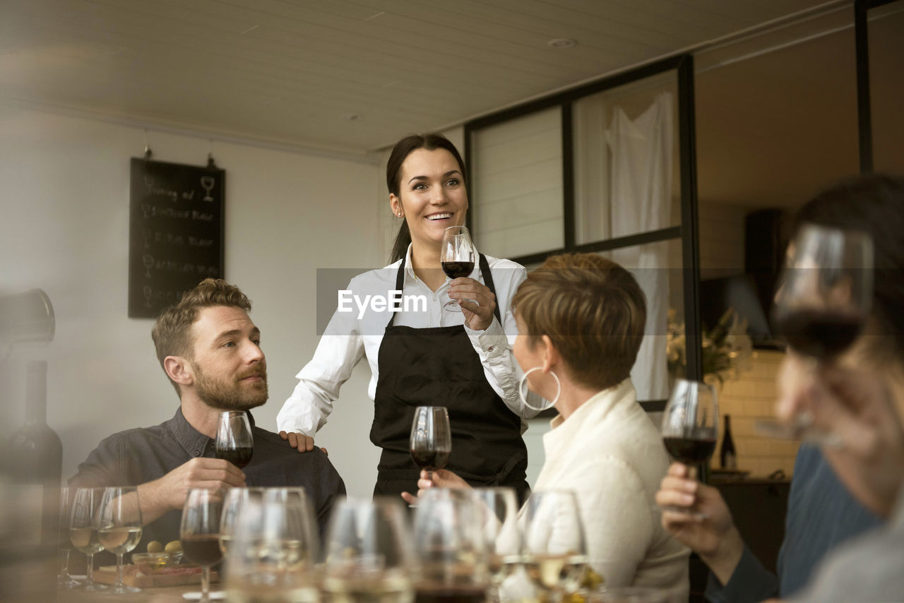 Smiling woman wearing apron holding wineglass with business people at table
