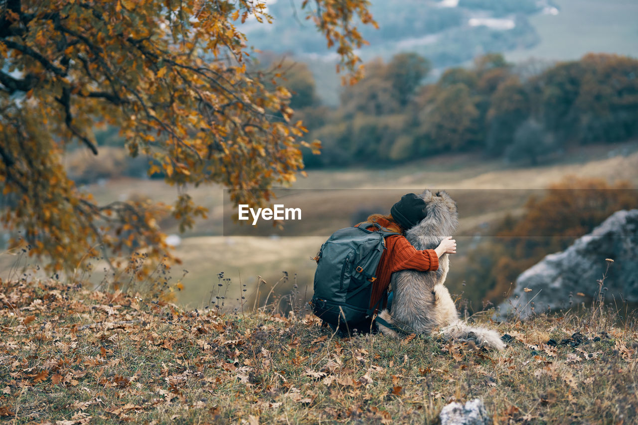 REAR VIEW OF MAN SITTING ON FIELD DURING AUTUMN