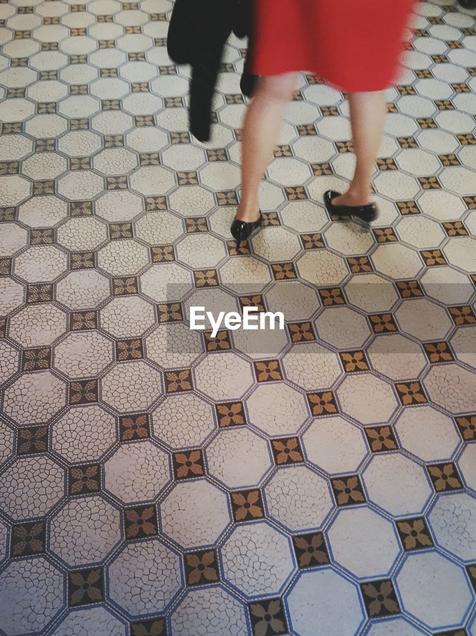 Low section of woman in red dress standing on patterned floor