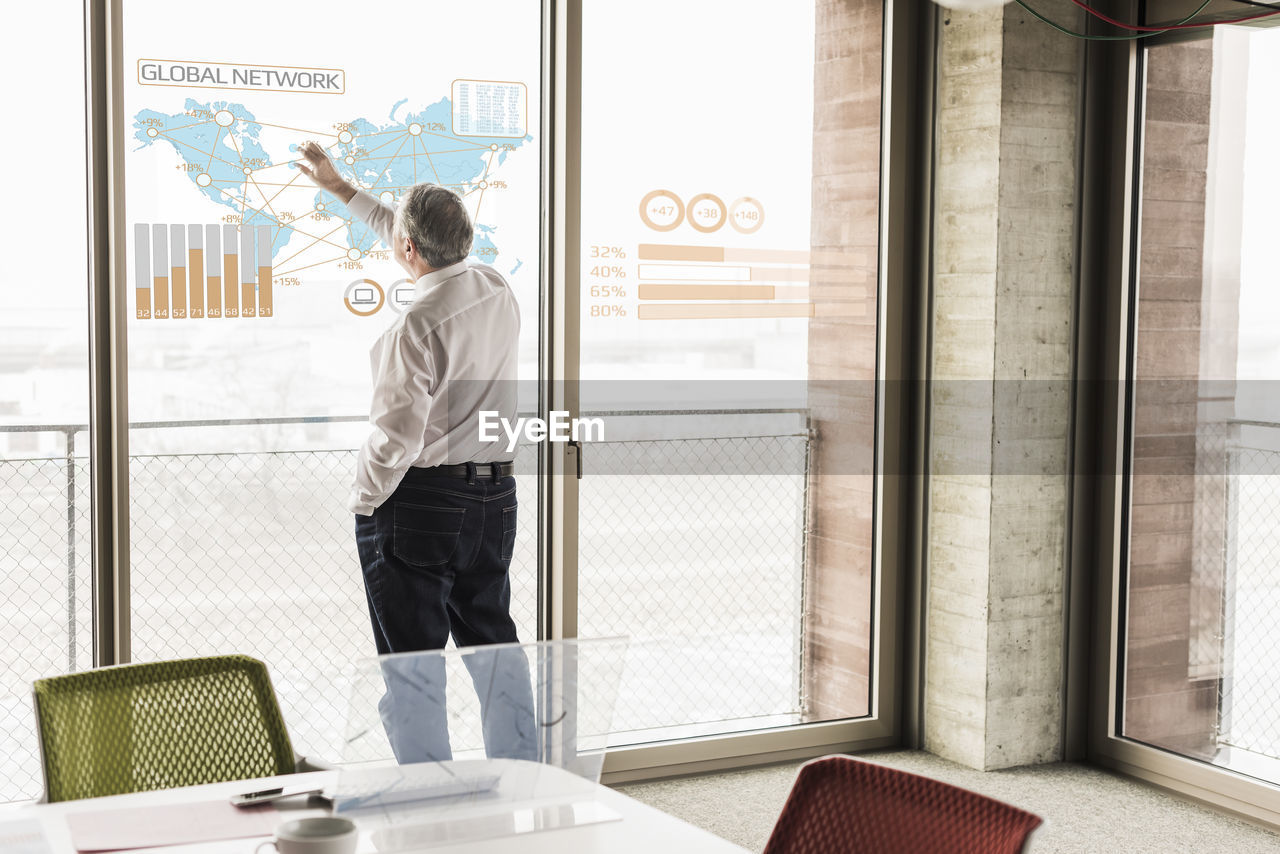 Businessman touching windowpane with world map and global network in office