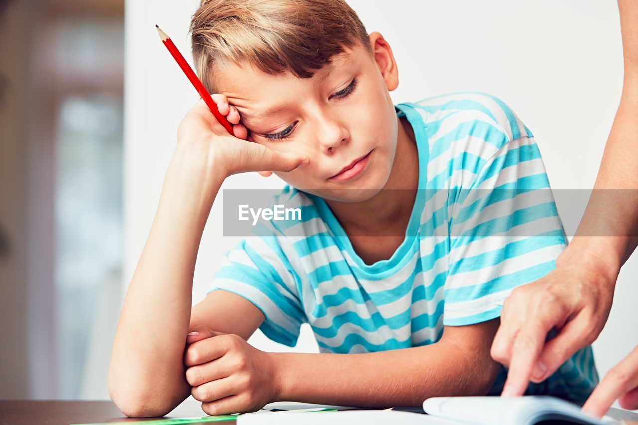 Cropped hand of mother assisting son in studying at home