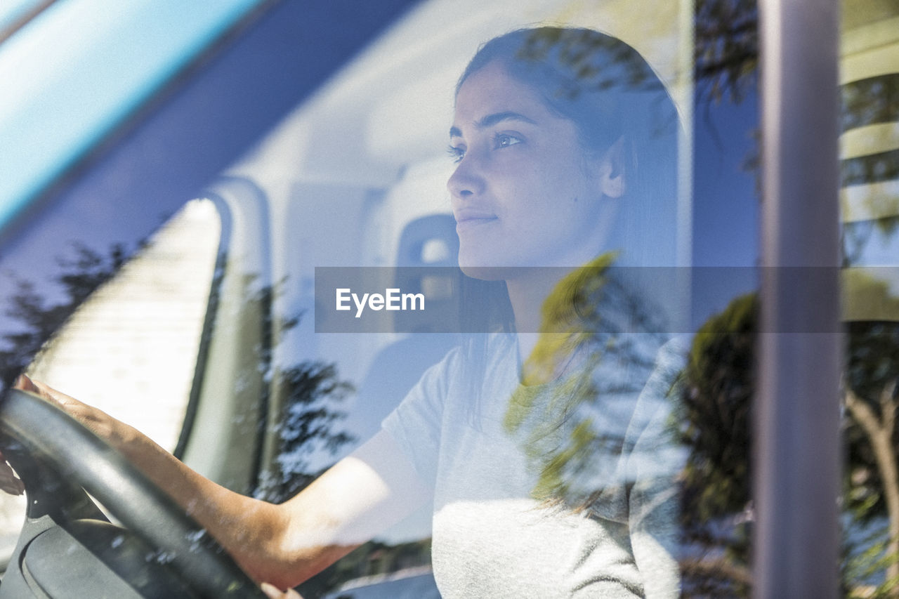 Confident young female owner driving food truck seen through window