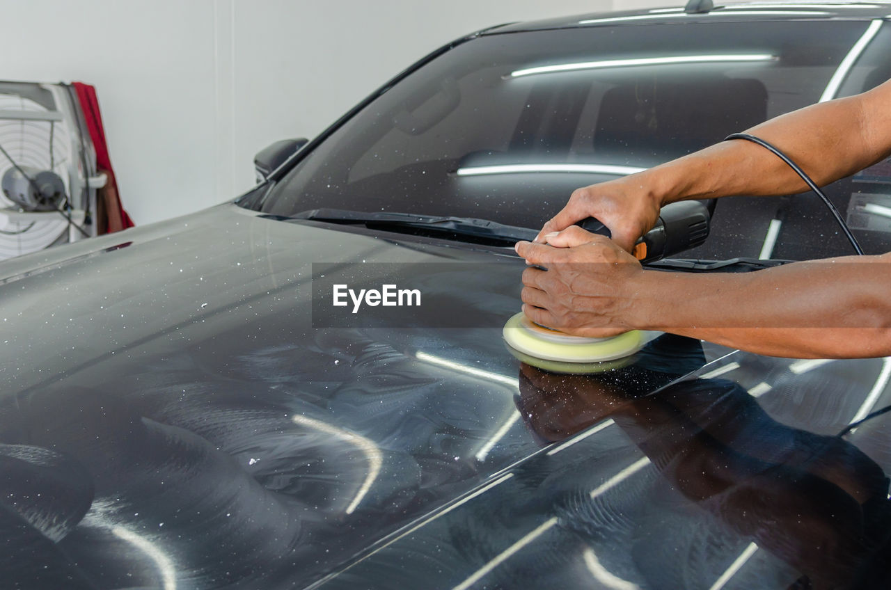 Cropped hands of mechanic polishing car in garage