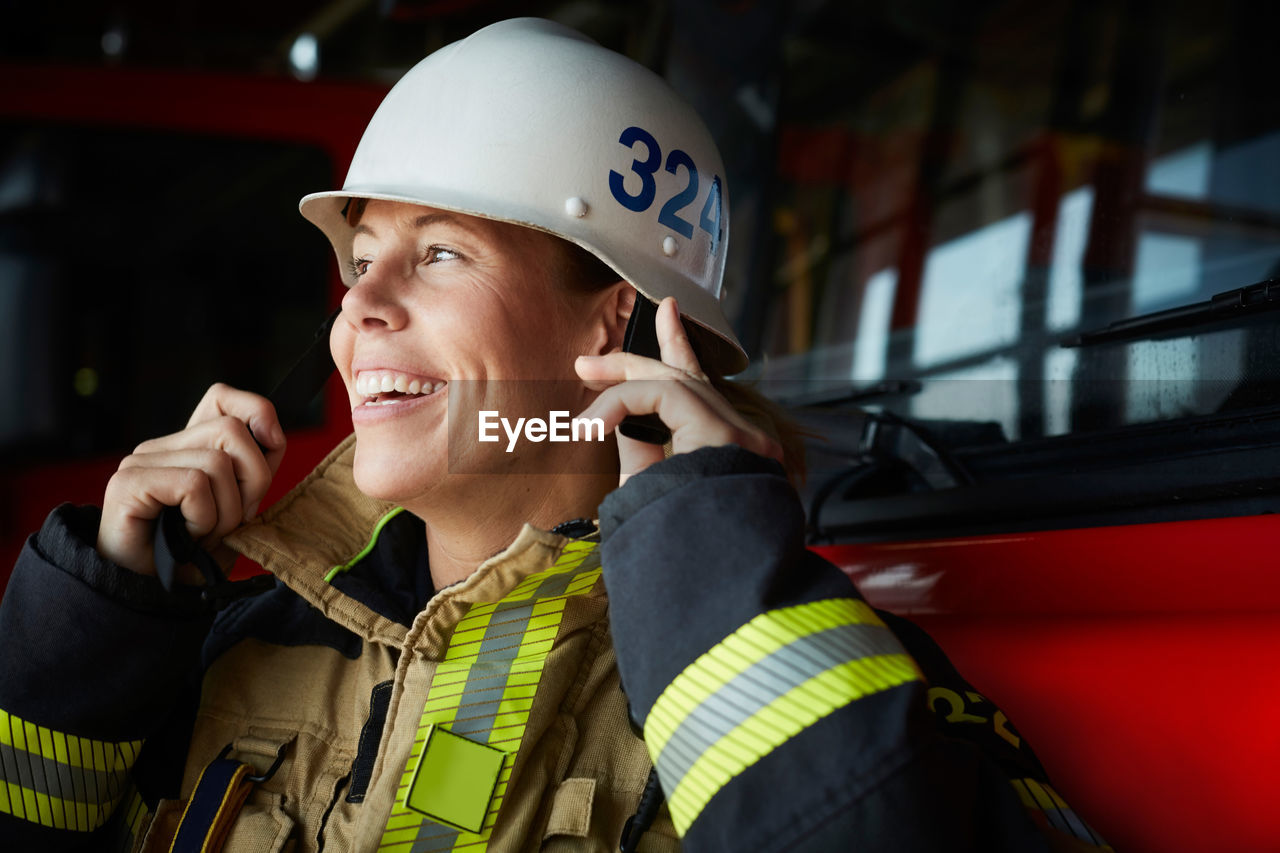 Smiling female firefighter wearing helmet at fire station