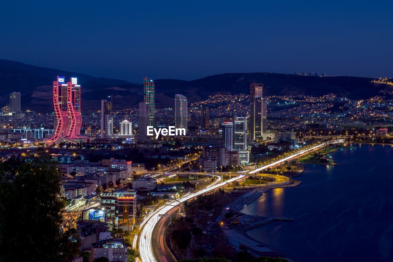 Illuminated city by buildings against clear sky at night