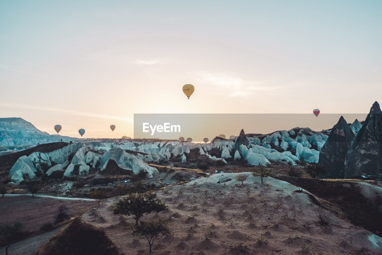 HOT AIR BALLOONS FLYING OVER ROCK FORMATION AGAINST SKY