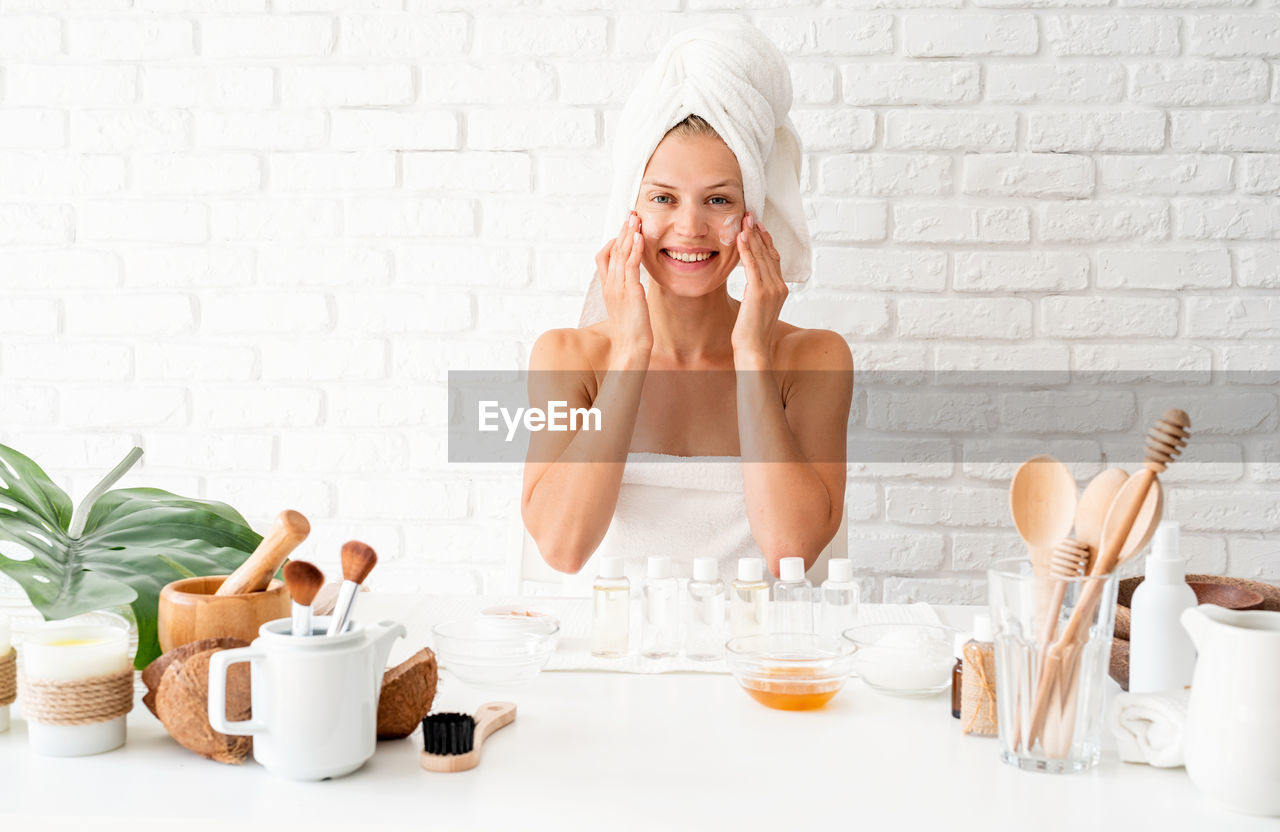 Happy young woman wearing white bathrobes towels on head doing spa procedures in spa beauty salon