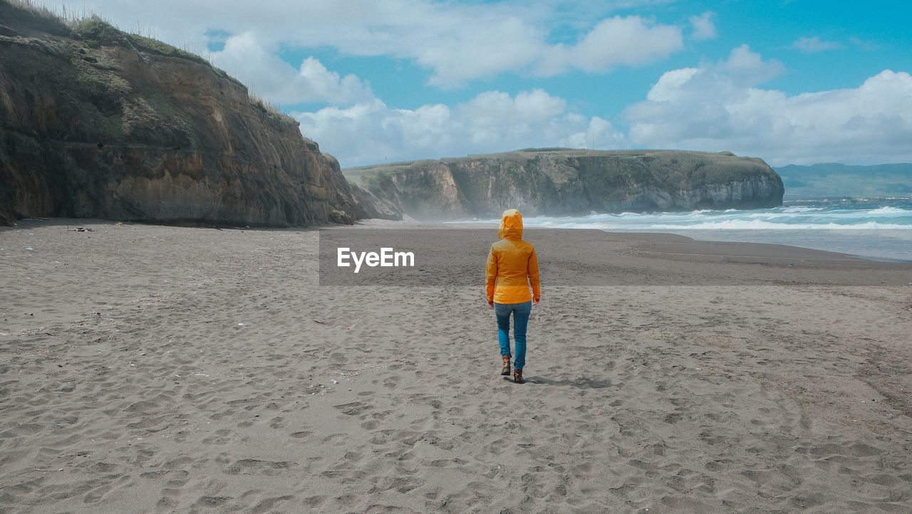 Rear view of woman walking at beach against sky