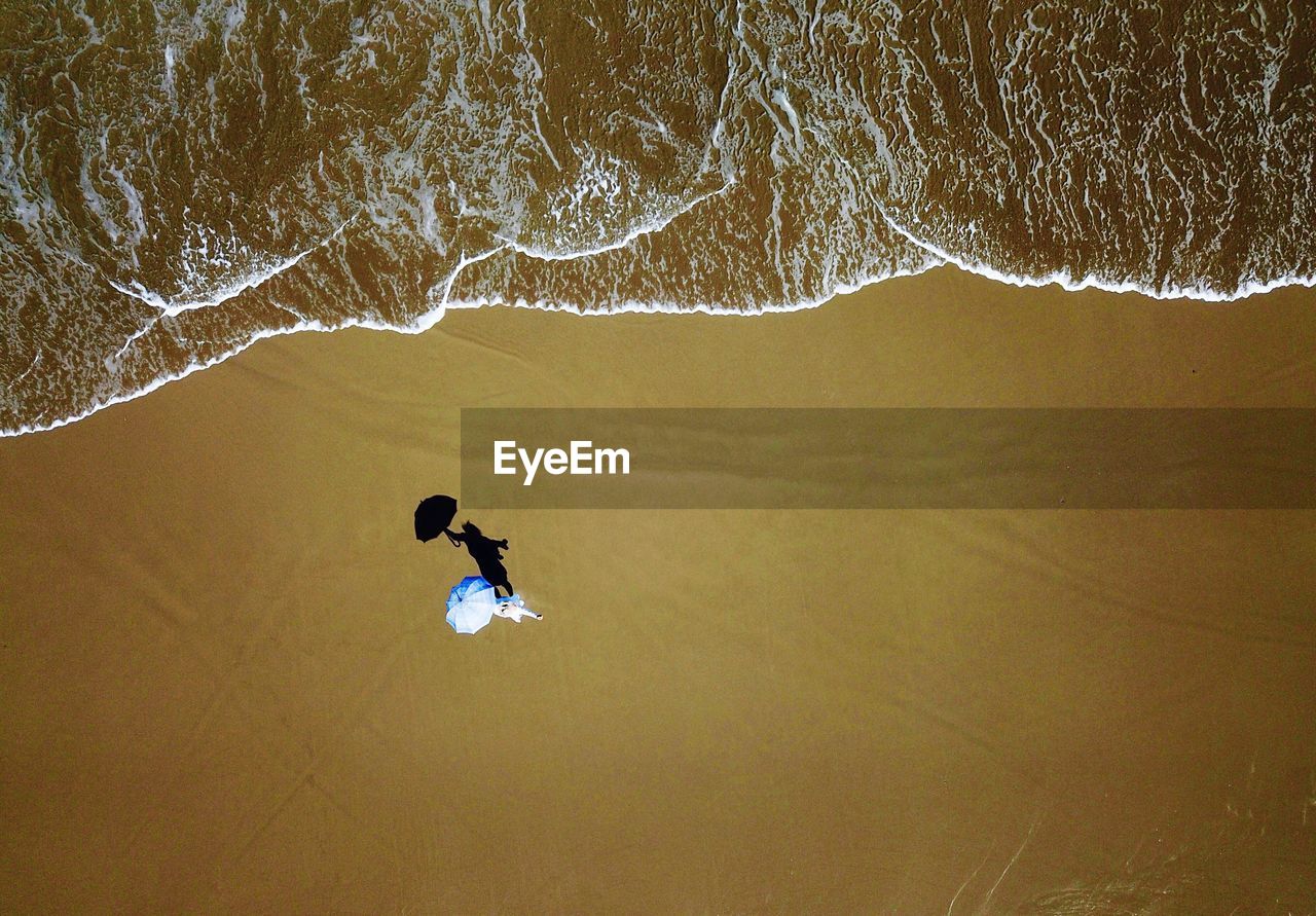 Aerial view of woman with umbrella standing at sandy beach