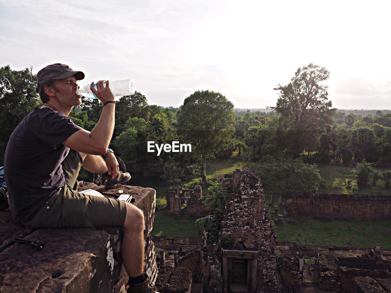 Male explorer drinking water against forest trees