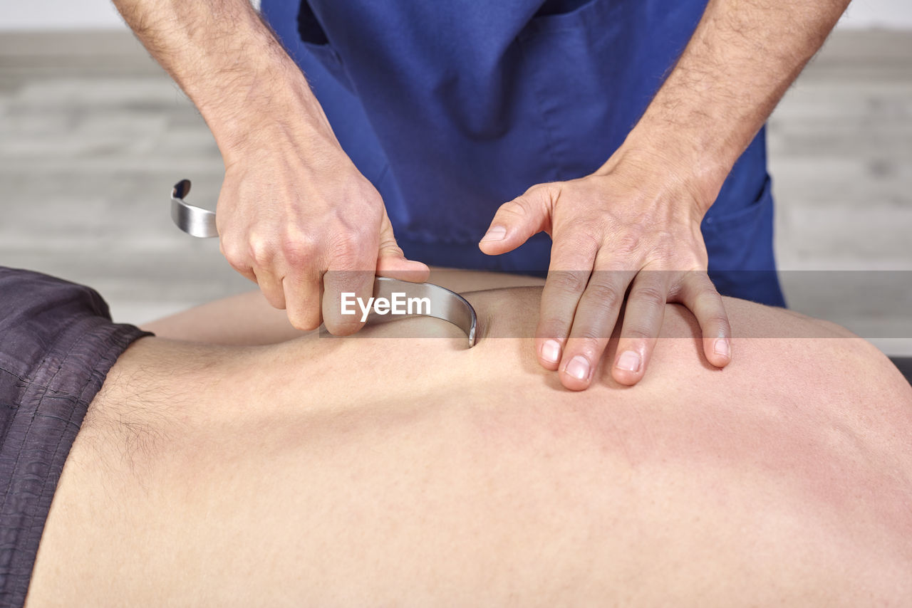 Midsection of man giving osteopath treatment with hook to patient lying at clinic