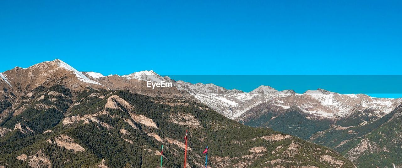 Low angle view of snowcapped mountains against clear blue sky