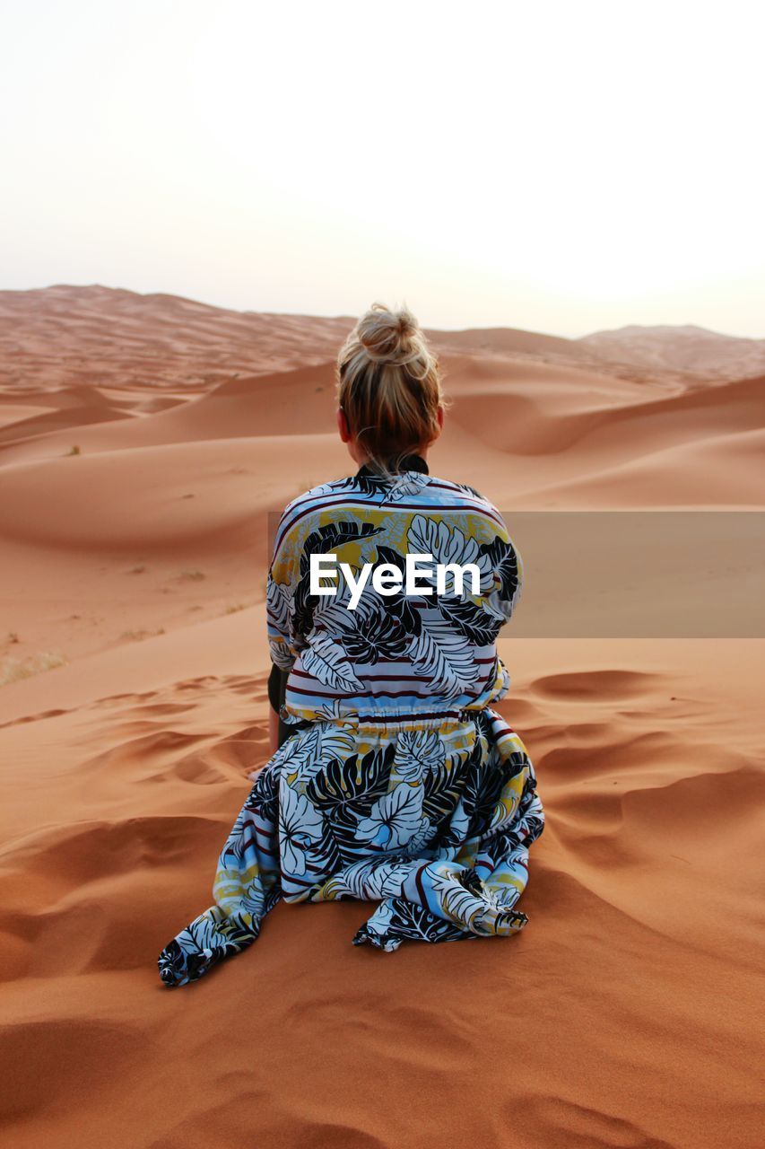 Rear view of woman sitting on sand dune
