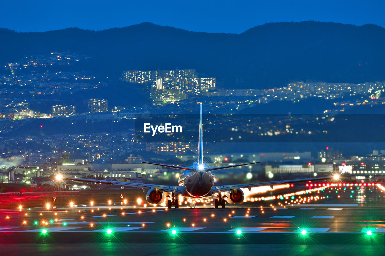 Airplane landing on runway in illuminated city against sky at night