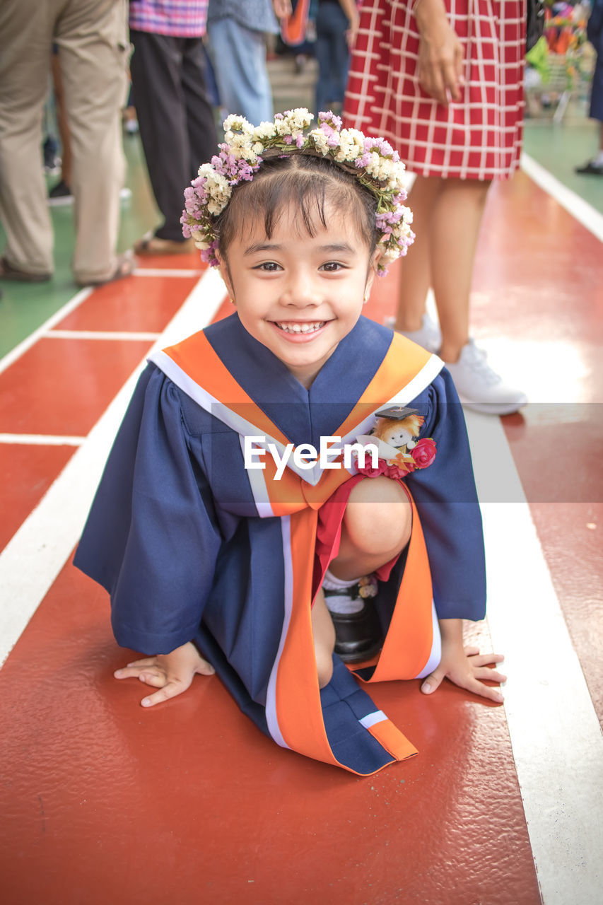 Portrait of smiling girl wearing flowers while kneeling on floor