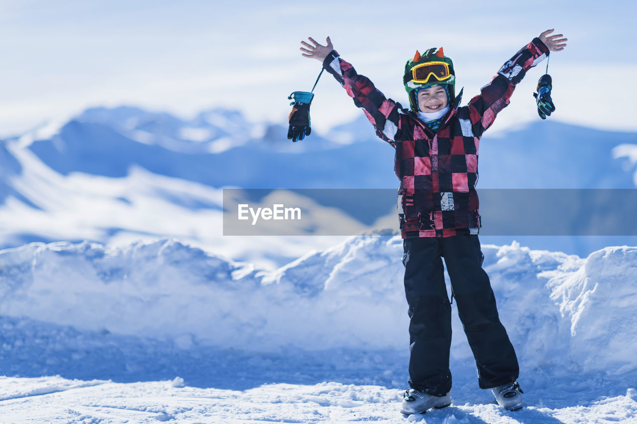 Portrait of happy boy with arms outstretched standing against snowcapped mountains