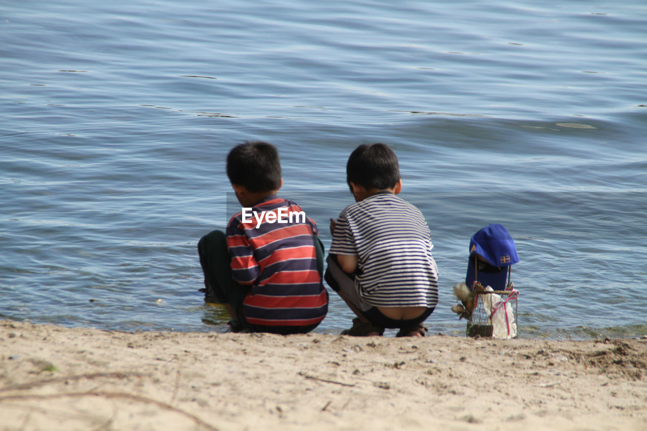 REAR VIEW OF TWO MEN SITTING ON SHORE