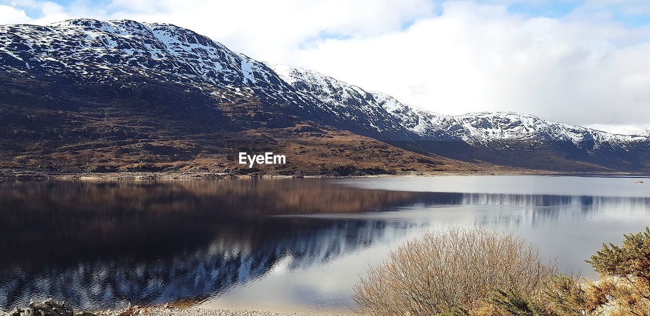 Scenic view of lake by snowcapped mountains against sky