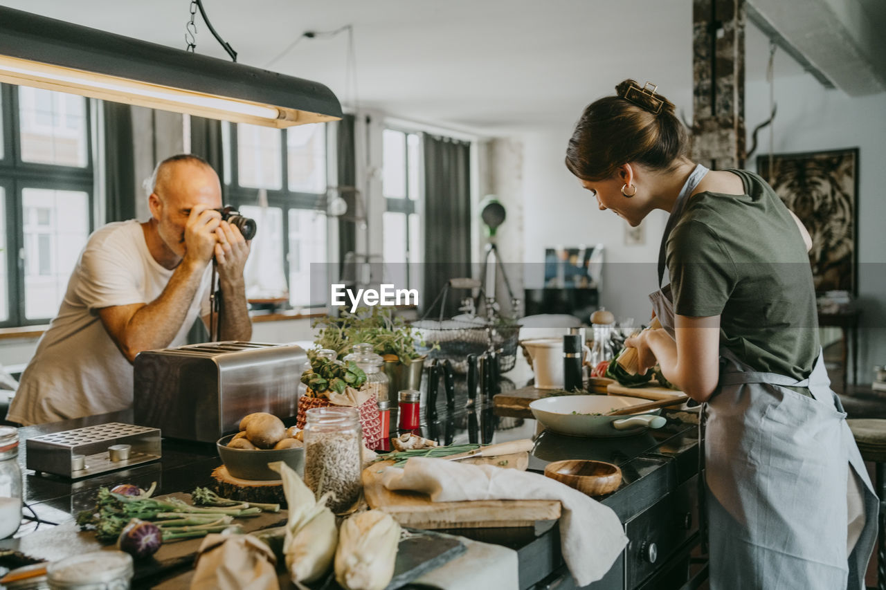 Photographer clicking picture of chef preparing food in studio kitchen