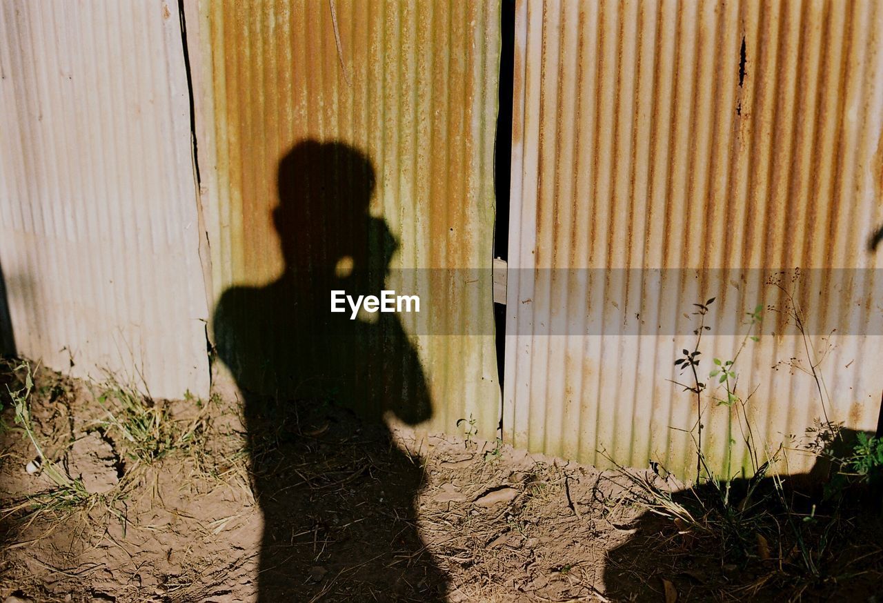 Shadow of man photographing corrugated iron fence