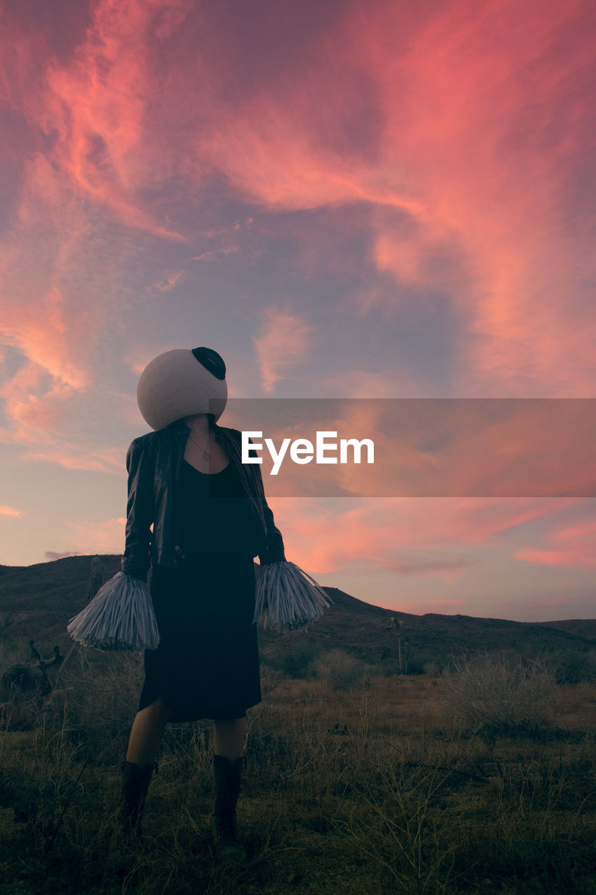 Woman wearing costume while standing on grass against sky during sunset