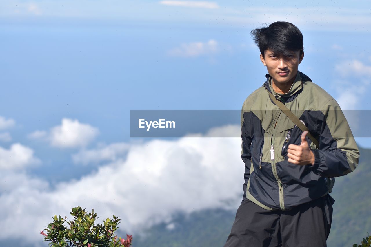 Portrait of young man gesturing thumbs up on mountain against sky