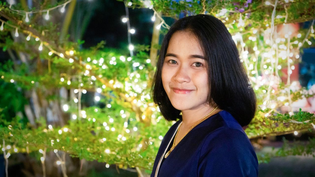 Portrait of smiling young woman standing against illuminated trees 