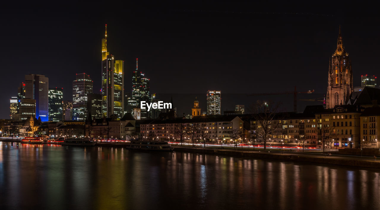 Illuminated buildings by river against sky in city at night