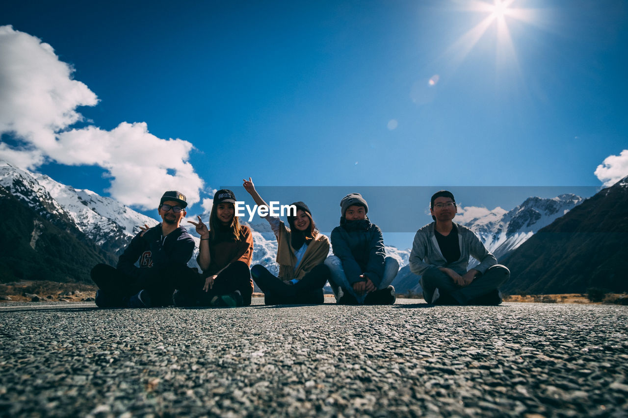 PEOPLE SITTING ON MOUNTAIN AGAINST SKY