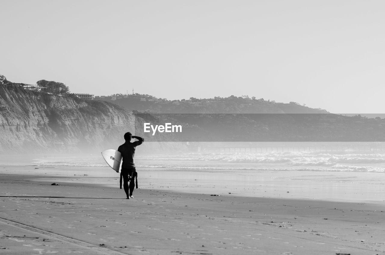 Rear view of man walking with surfboard at beach