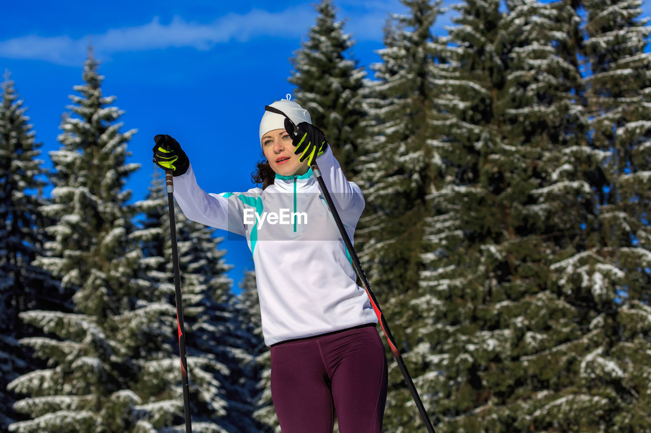 Low angle view of mid adult woman skiing against trees in forest