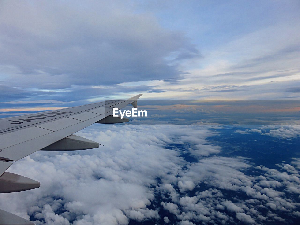 CROPPED IMAGE OF AIRPLANE WING OVER CLOUDS