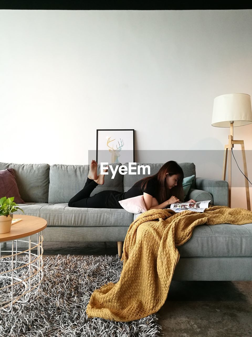 YOUNG WOMAN USING MOBILE PHONE ON SOFA AT HOME