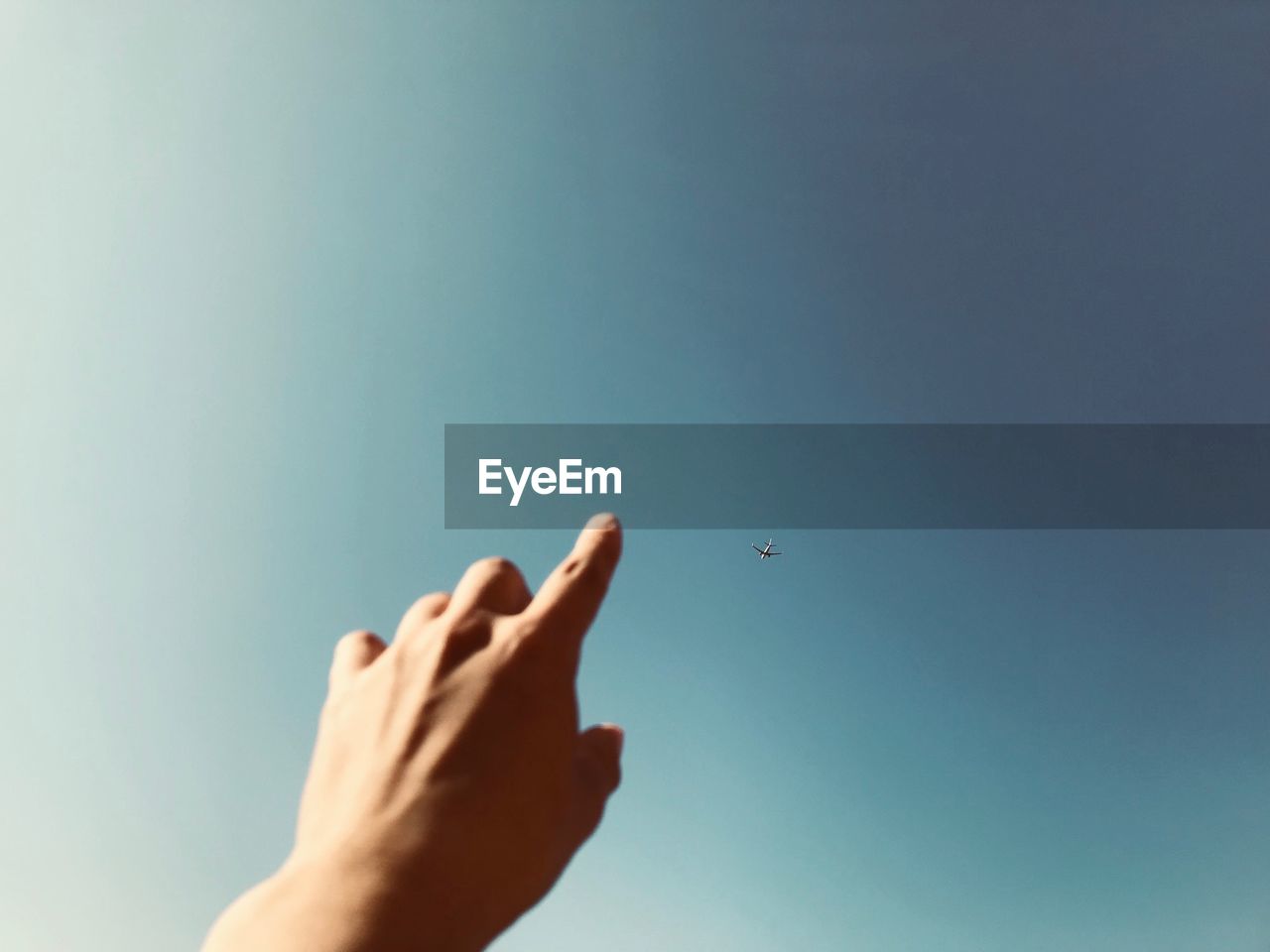 Cropped hand pointing at airplane flying against clear sky