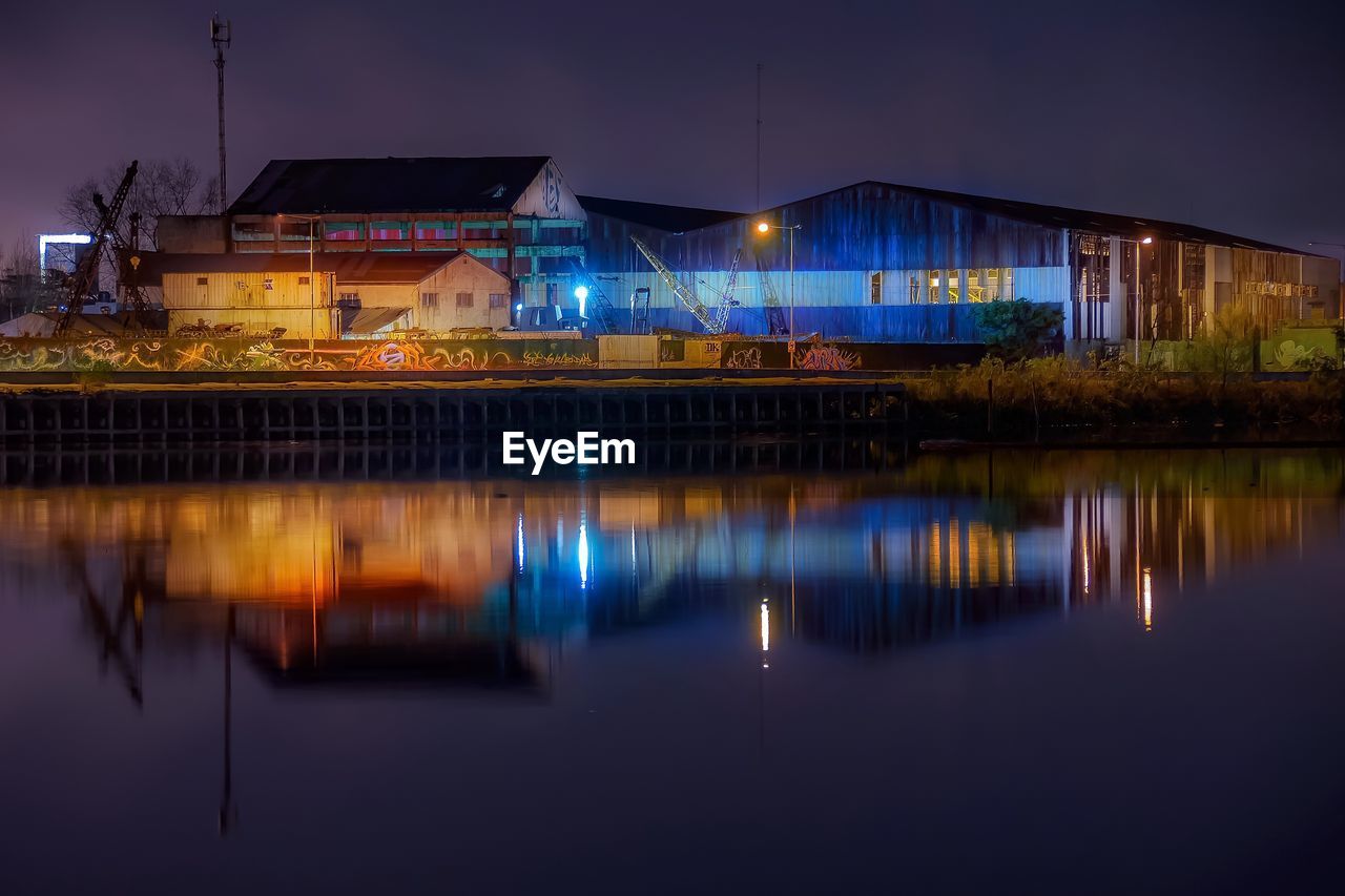 Illuminated industrial buildings with reflection on lake at night