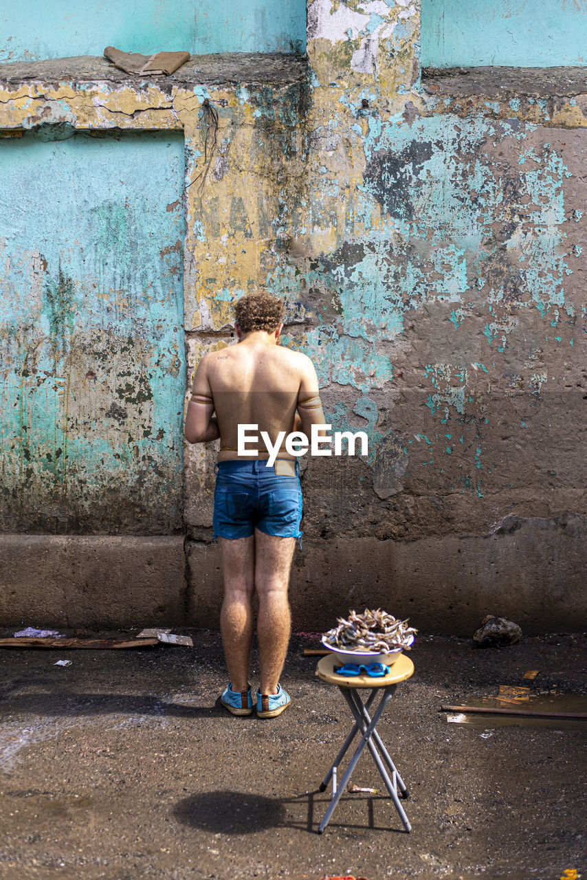 Rear view of shirtless man standing against wall