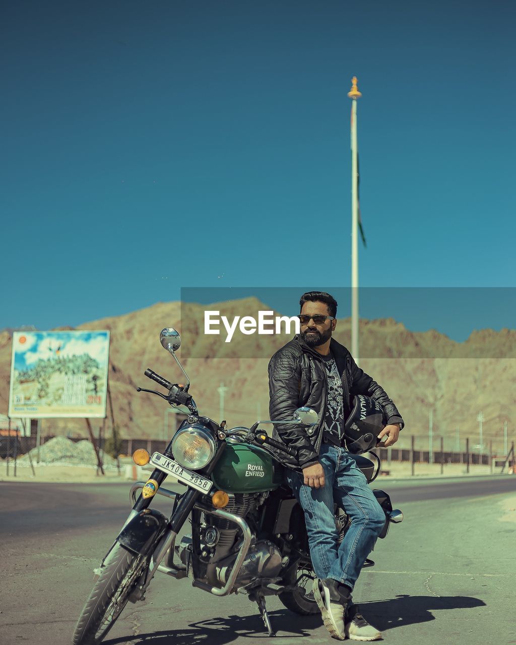 Full length of man leaning on motorcycle against blue sky