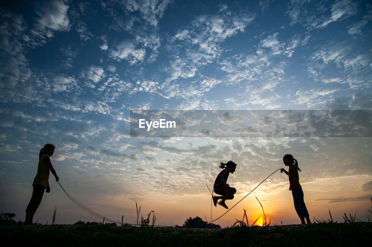 Silhouette people playing soccer against sky during sunset